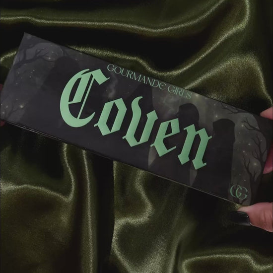 Video of the Coven palette opened on olive satin, then each shade swatched one by one on a light-skinned arm beside the box