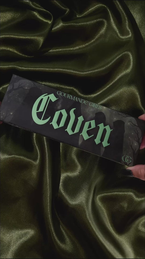 Video of the Coven palette opened on olive satin, then each shade swatched one by one on a light-skinned arm beside the box