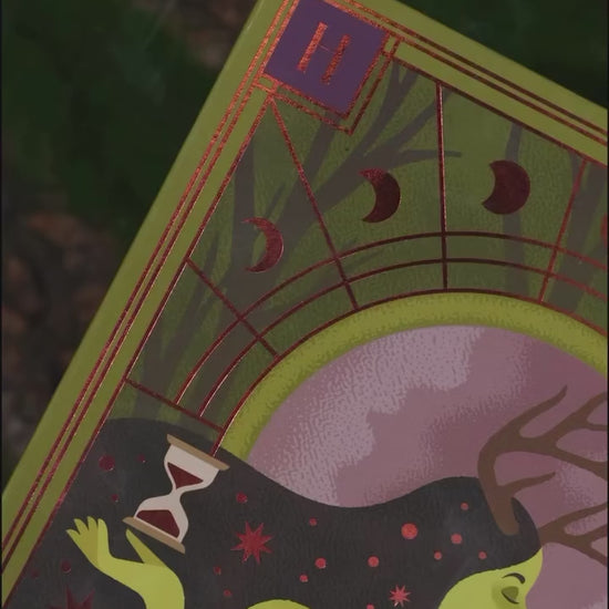 Video of The Huldra palette packaging close-up: a green-skinned figure with antlers holding an hourglass, framed by red copper moon phases