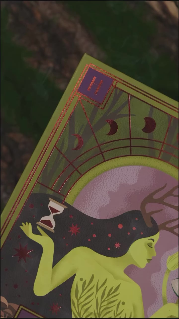 Video of The Huldra palette packaging close-up: a green-skinned figure with antlers holding an hourglass, framed by red copper moon phases