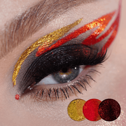 Graphic eye look with gold, orange and red flame strokes over a black winged lid, gold, red and dark red sparkle dots below.