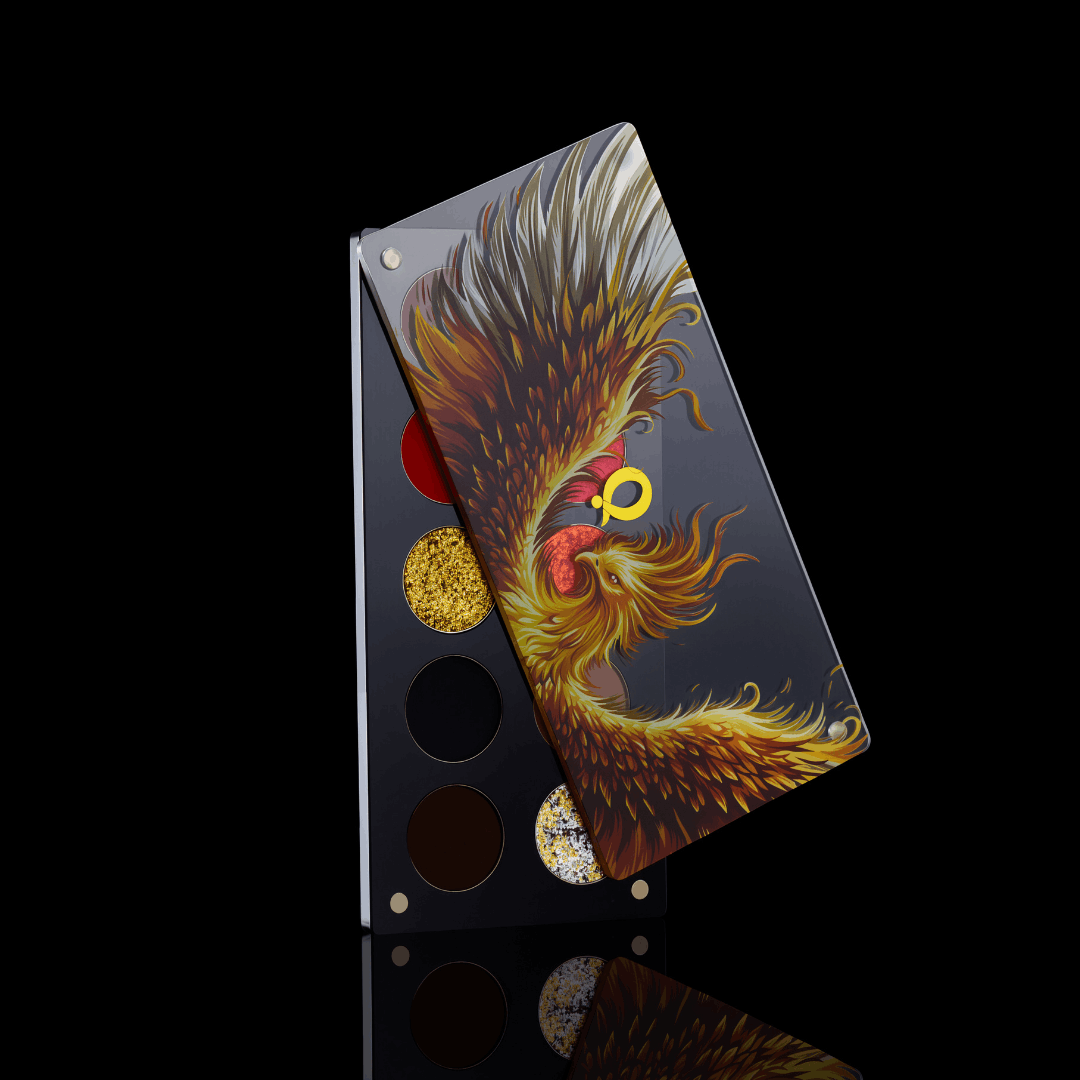 Question Beauty Wings of Fire and Gold eyeshadow palette with the phoenix lid half open over the pans, standing on a black reflective surface.