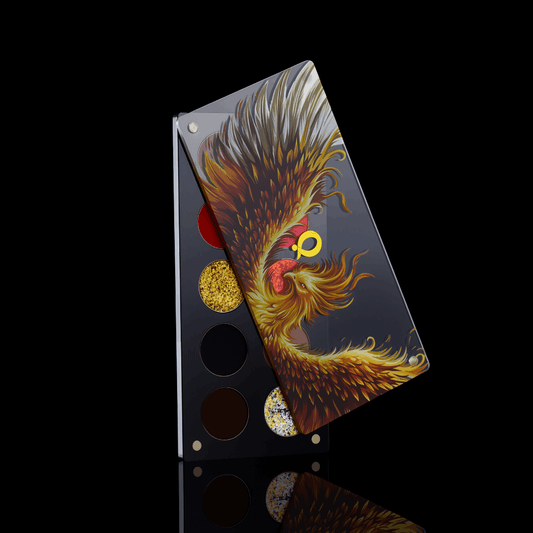Question Beauty Wings of Fire and Gold eyeshadow palette with the phoenix lid half open over the pans, standing on a black reflective surface.