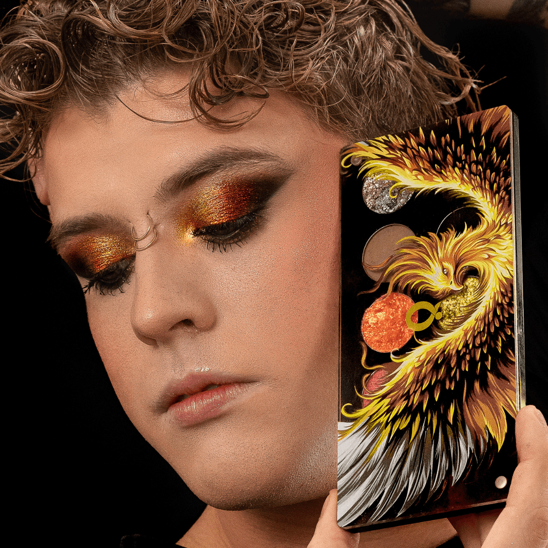 Model with a copper and orange shimmer eye look holding the closed palette upright against the cheek.