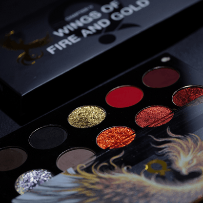 Angled close-up of the pans, from lilac sparkle and greys up to gold, orange and reds, with the black box and its title behind.
