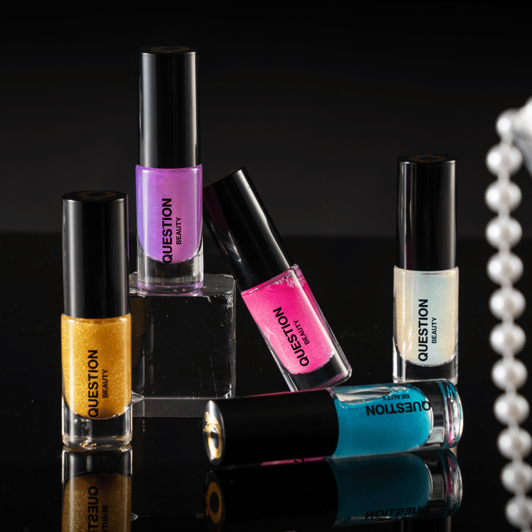 Five mini bottles in gold, purple, pink, pearl and teal standing on a black surface, a pearl strand to the right.