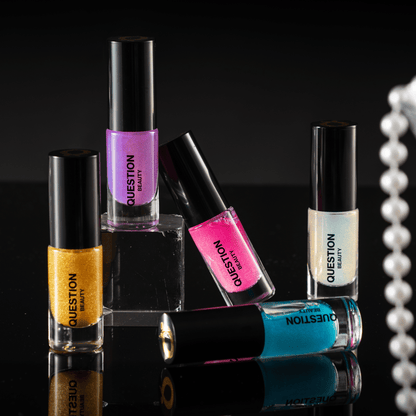 Five mini bottles in gold, purple, pink, pearl and teal standing on a black surface, a pearl strand to the right.