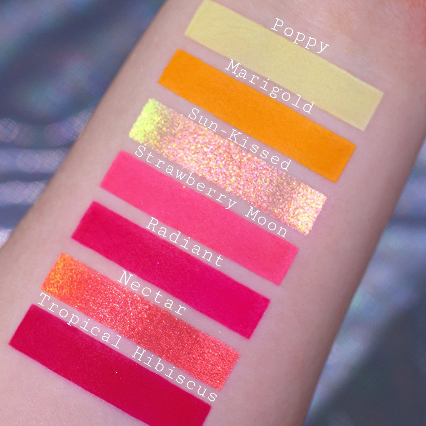 Seven bright shades swatched on light skin: Poppy, Marigold, Sun-Kissed, Strawberry Moon, Radiant, Nectar, and Tropical Hibiscus