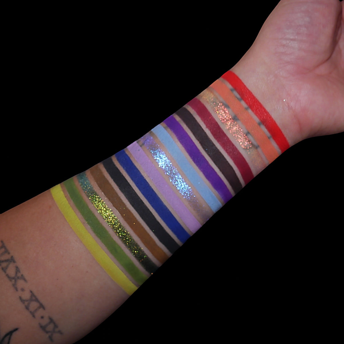 All 15 shades swatched on a light-skinned forearm, neon yellow and olive through blues and purples to burgundy, orange and red, with three sparkly stripes