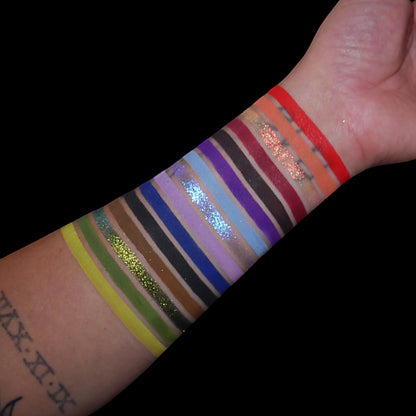 All 15 shades swatched on a light-skinned forearm, neon yellow and olive through blues and purples to burgundy, orange and red, with three sparkly stripes