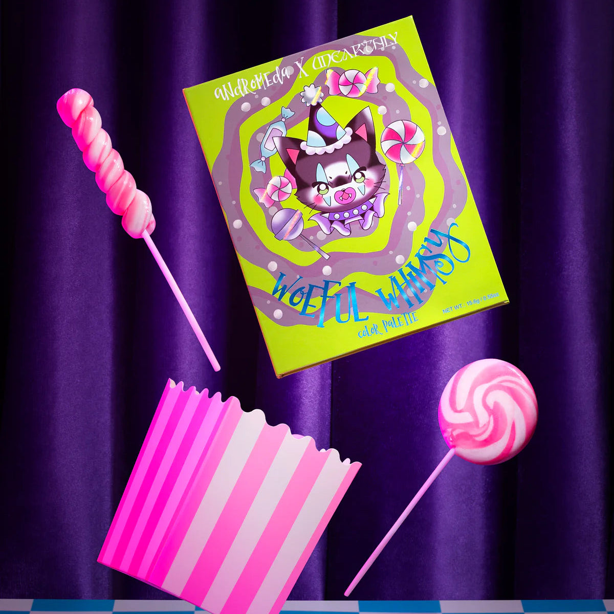 Woeful Whimsy palette by Unearthly Cosmetics - closed neon green box showing the Andromeda x Unearthly artwork and candy props against a purple draped backdrop
