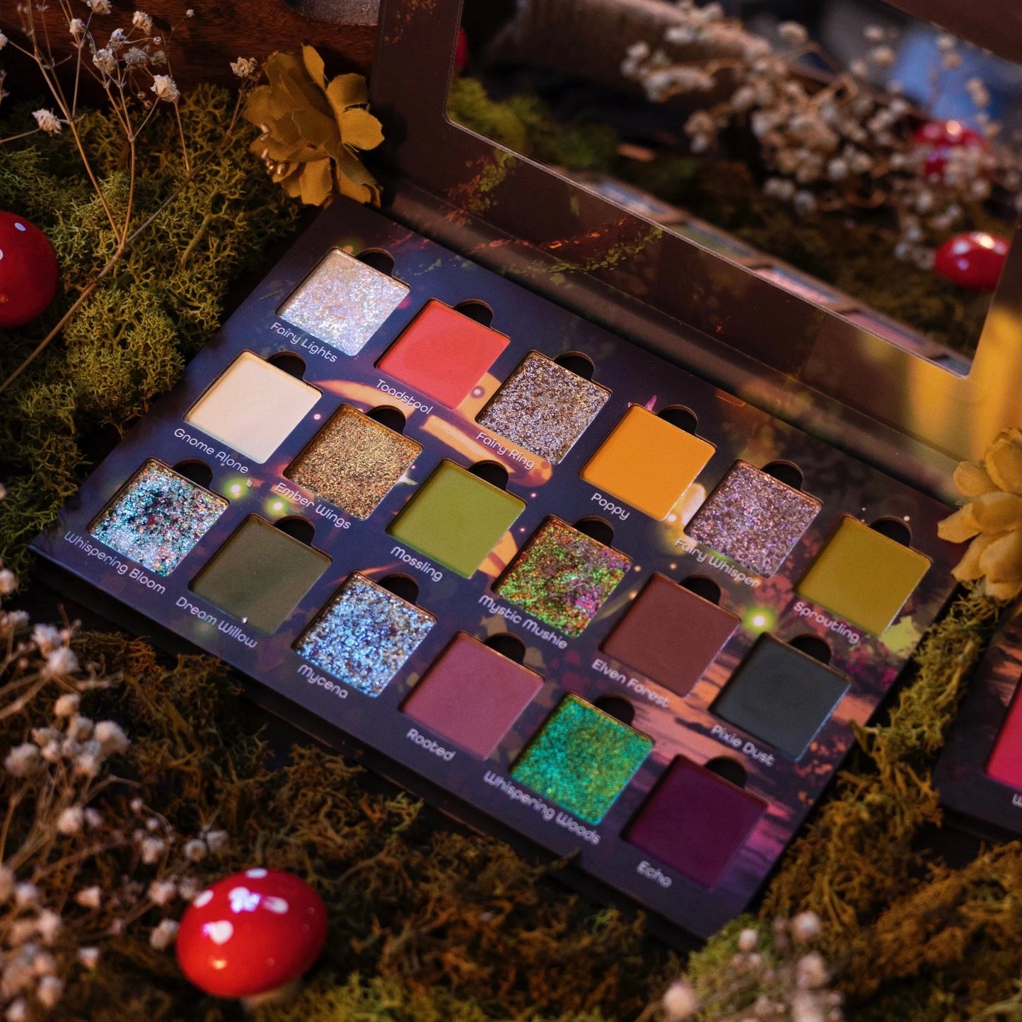 Ensley Reign Whispering Woods eyeshadow palette open among forest floor moss, red mushrooms, and dried botanicals, all 18 shades visible